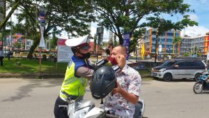 Salah seorang personel Sat Lantas Polres Nias, memasangkan masker kepada salah seorang pengendara pada Operasi Yustisi 2020, Senin (14/09/2020)/ foto: Humas Polres Nias